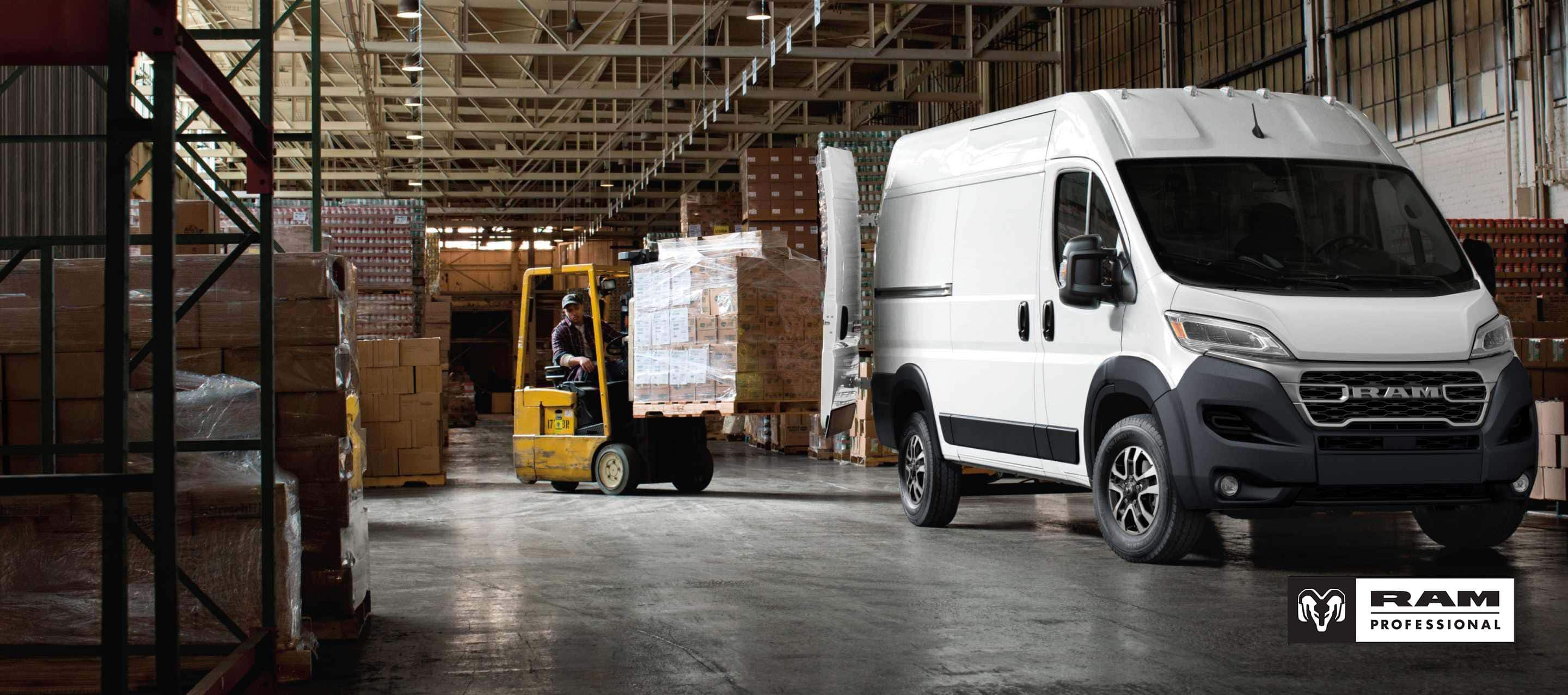 A passenger-side front angle of a white 2026 Ram ProMaster 2500 SLT Cargo Van High Roof, parked in a warehouse with its rear doors fully open and a forklift with a pile of boxes being driven toward the back of the van. Ram Professional.