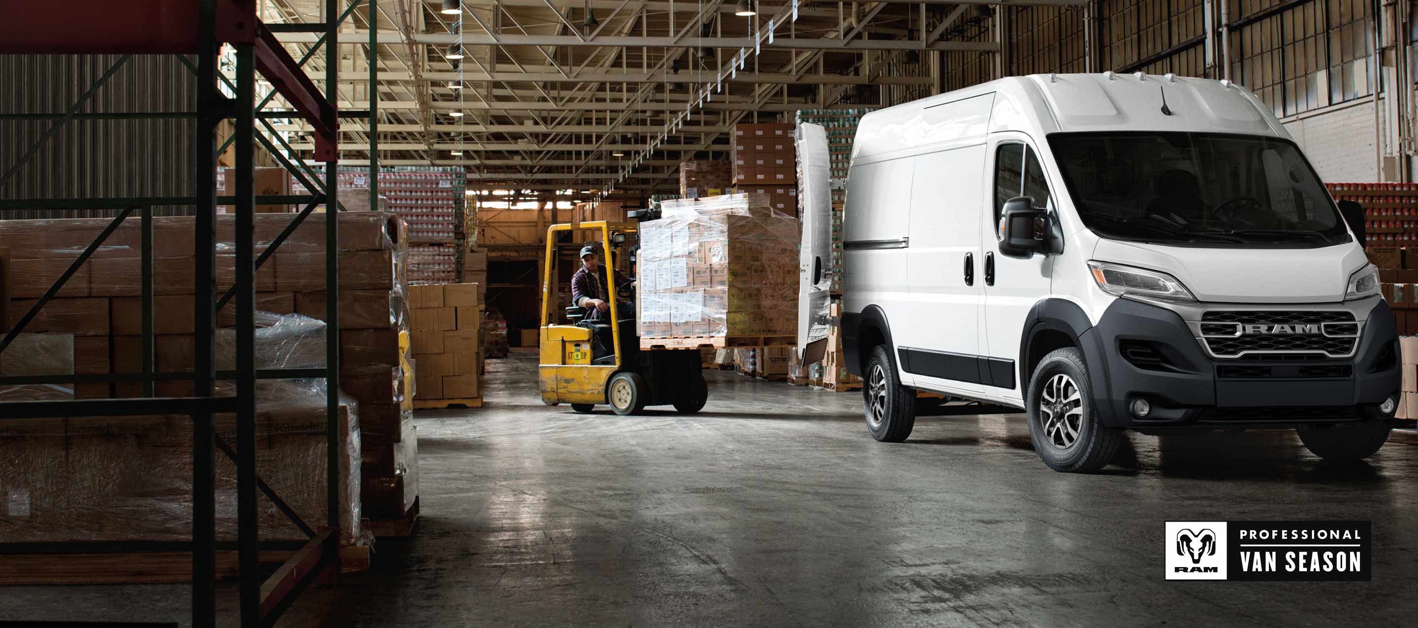 A passenger-side front angle of a white 2026 Ram ProMaster 2500 SLT Cargo Van High Roof, parked in a warehouse with its rear doors fully open and a forklift with a pile of boxes being driven toward the back of the van. Ram Professional Van Season.