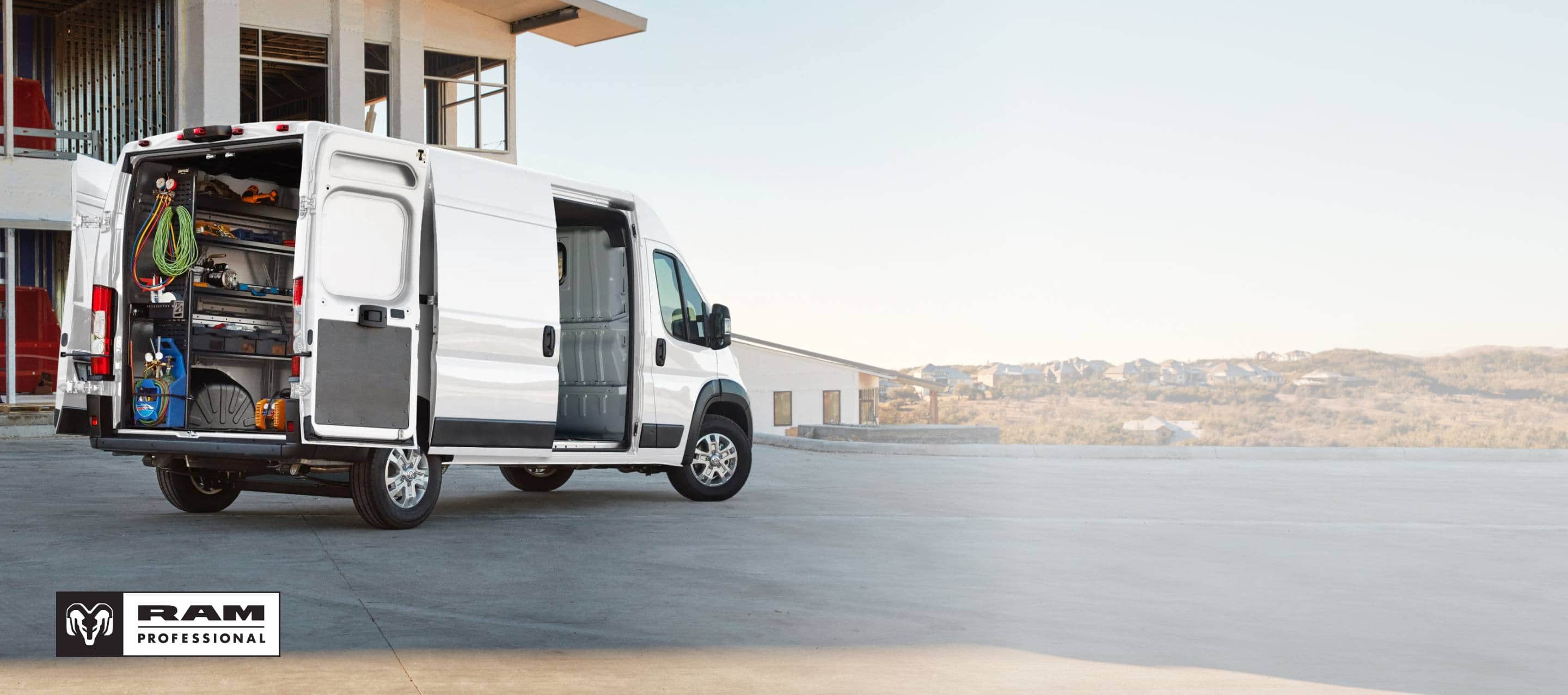 The rear of a white 2026 Ram ProMaster 3500 SLT High Roof Cargo Van with its passenger-side sliding door and rear doors open, displaying shelves full of tools. Ram Professional.