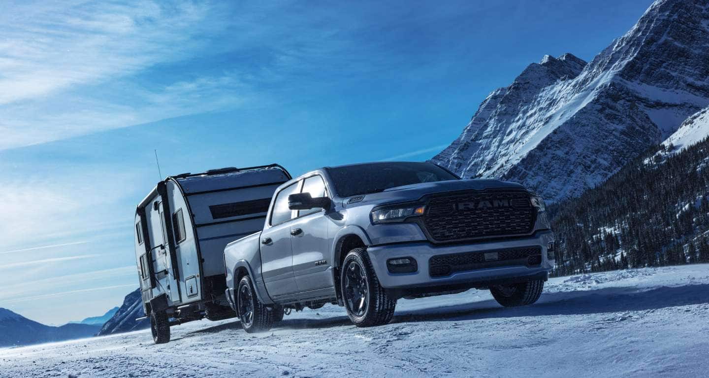A passenger-side front angle of a white 2027 Ram 1500 Big Horn 4x4 Crew Cab towing a travel trailer