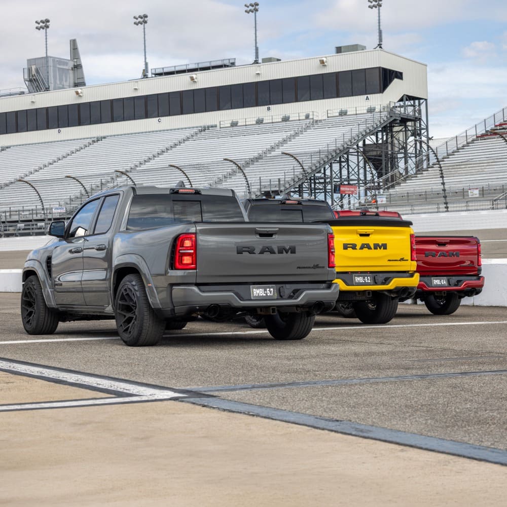 Three 2027 Ram 1500 Rumble Bee trucks at a racetrack, rear view