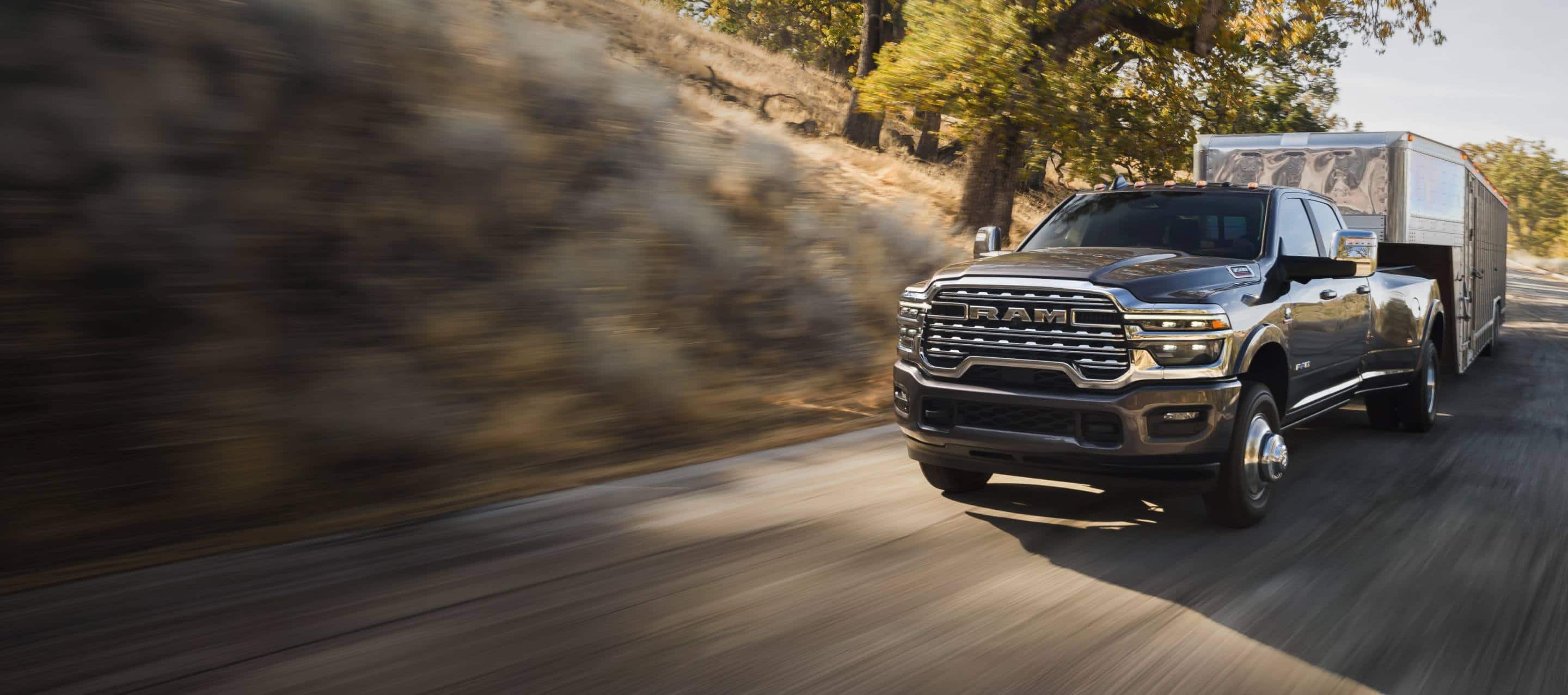 A gray 2027 Ram 3500 Heavy Duty Limited Longhorn 4x4 Crew Cab pickup truck traveling down a highway as it tows a large fifth-wheel livestock trailer. Power That Pulls Through.