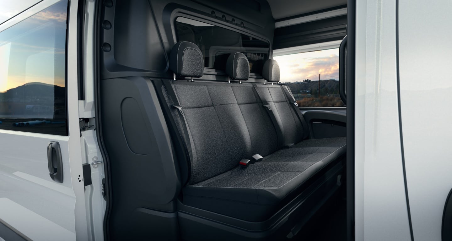 Display The rear seats in a white 2027 Ram ProMaster 2500 Tradesman High Roof Cargo Van with the Crew Van Package, shot through the open passenger-side sliding door.