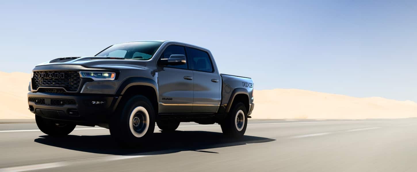 A gray 2027 Ram 1500 RHO 4x4 Crew Cab traveling down a highway in the desert.
