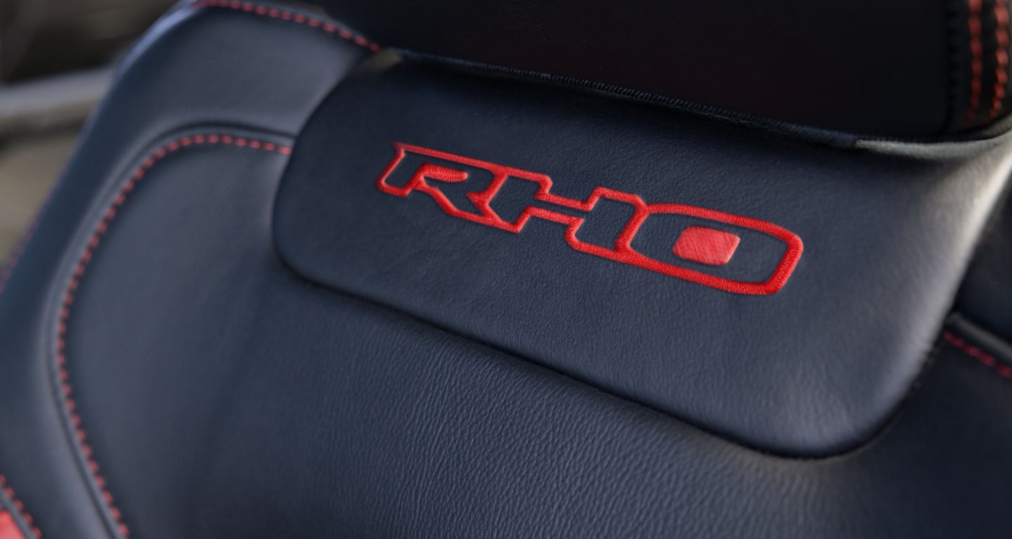 Display RHO lettering embroidered in red stitching just below the headrest of the driver seat in the 2027 Ram 1500 RHO 4x4 Crew Cab.