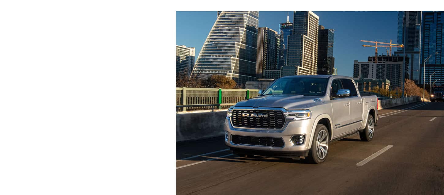 A silver 2025 Ram Tungsten Crew Cab traveling across a bridge in the downtown business district of a city.