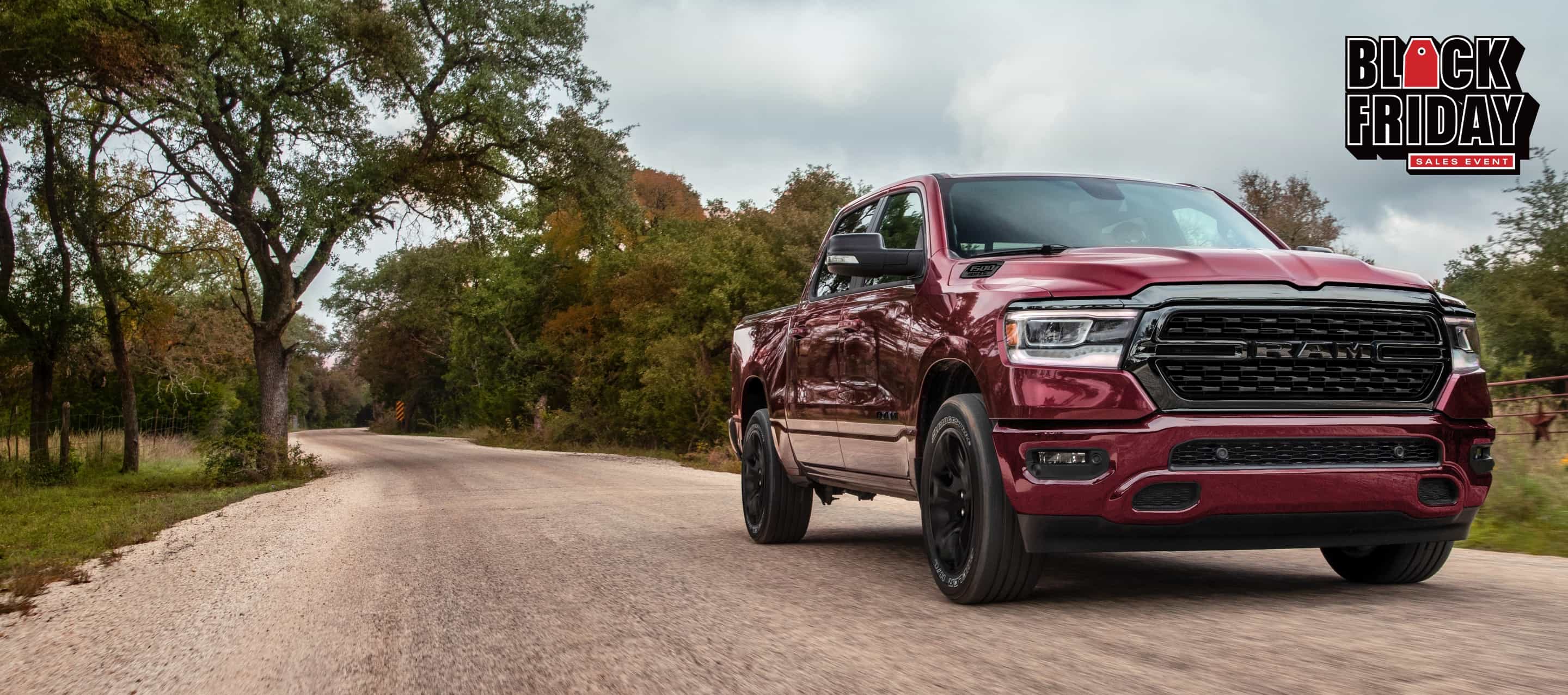 A red 2022 Ram 1500 Big Horn Crew Cab 4x4 being driven down a country road. The Black Friday Sales Event.