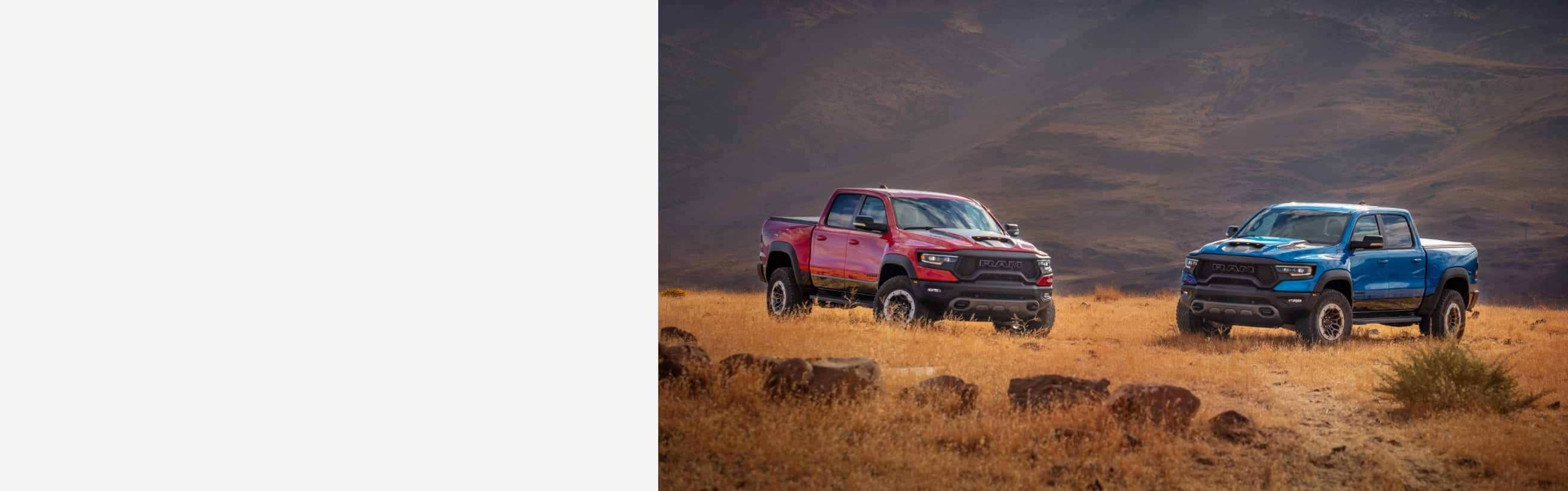 Two 2021 Ram 1500 TRX trucks parked in a field at the foot of a mountain.