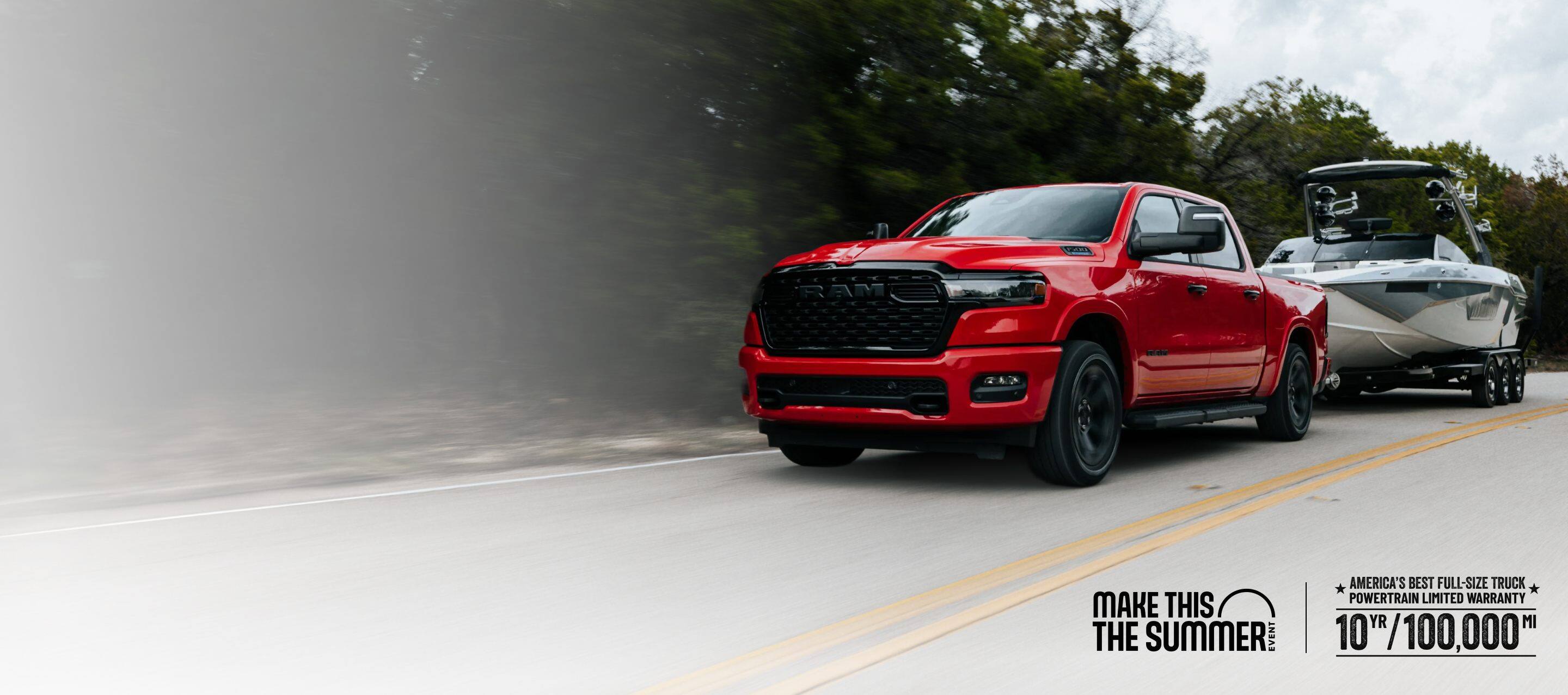 A red 2026 Ram 1500 Big Horn 4x4 Crew Cab pickup traveling down a highway, towing a motorboat. Limited Warranty—10 Years/100,000 Miles. Make This The Summer.