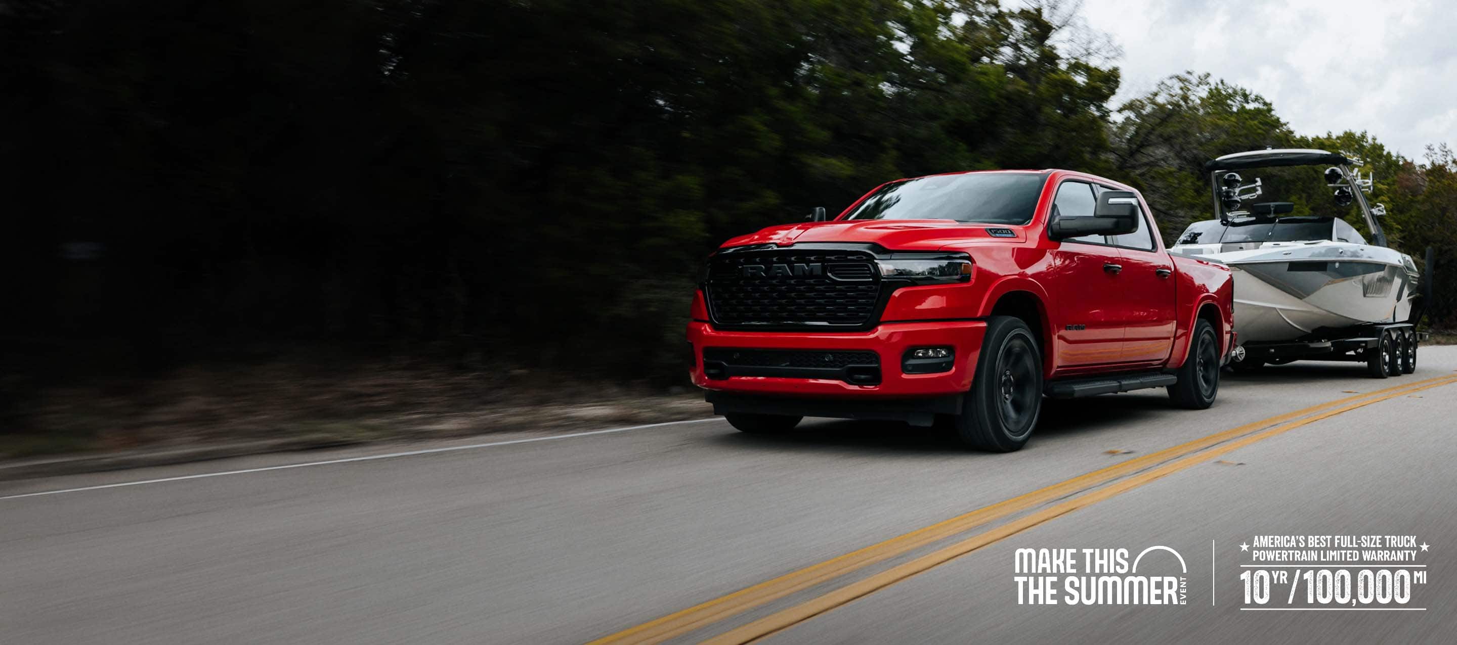 A red 2026 Ram 1500 Big Horn 4x4 Crew Cab pickup traveling down a highway, towing a motorboat. Limited Warranty—10 Years/100,000 Miles. Make This The Summer.