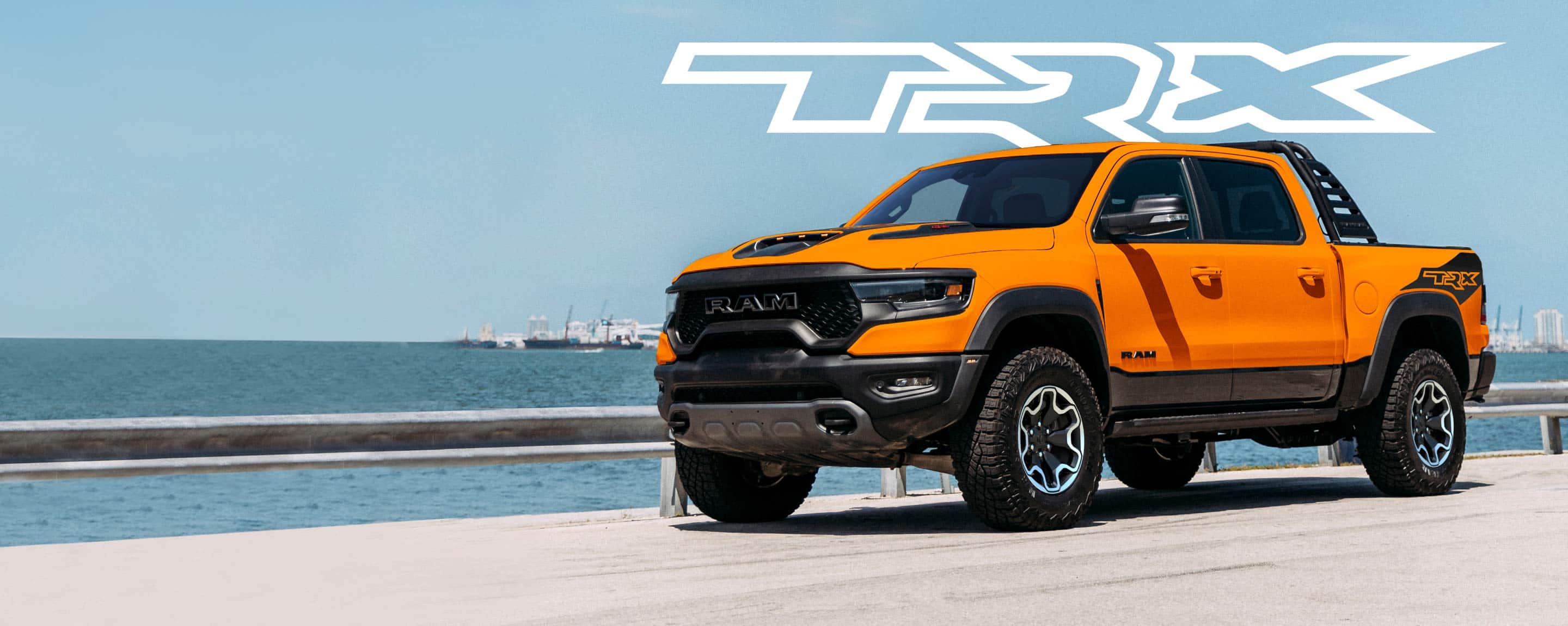An orange 2022 Ram 1500 TRX Ignition Edition parked in a seaside city lot with the TRX logo overhead.