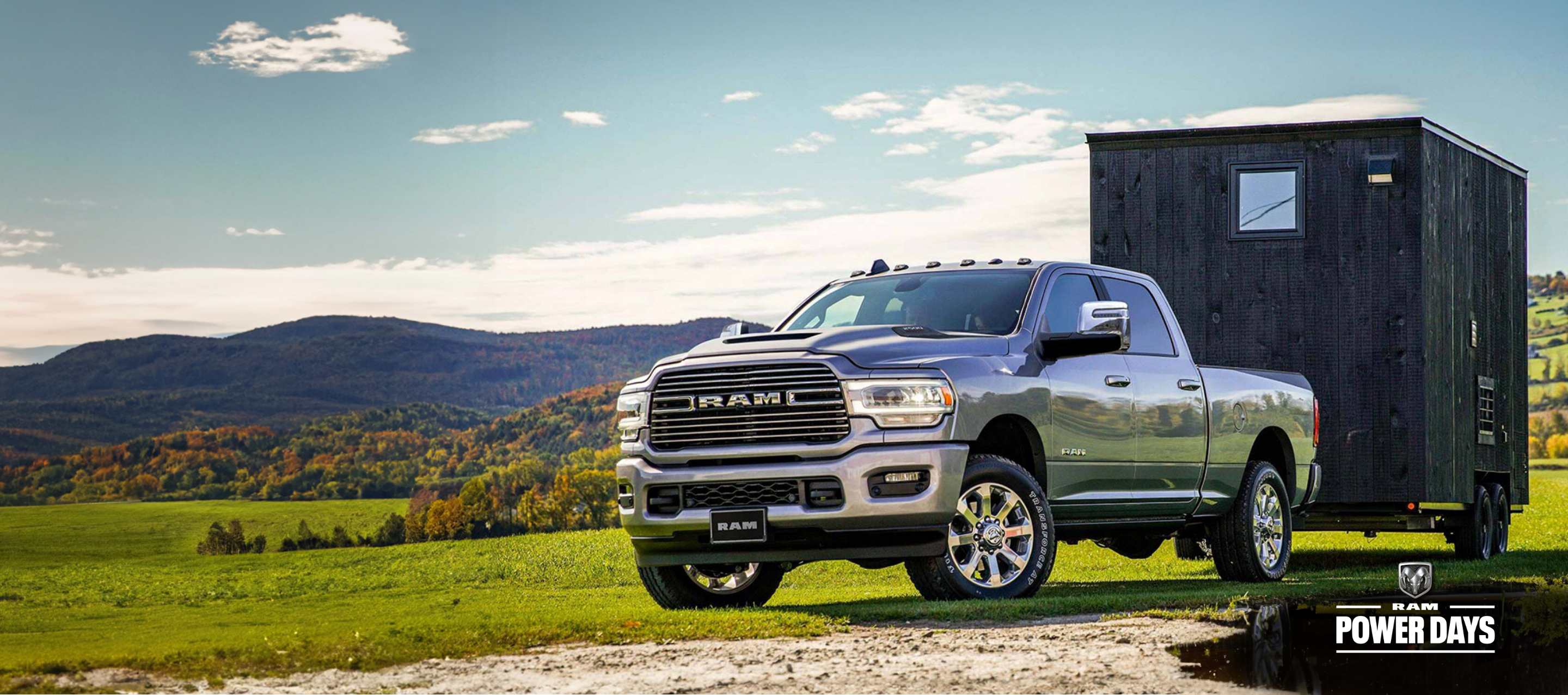 A 2023 Ram 2500 Laramie 4x4 Crew Cab towing a trailer parked on a grassy trail off-road. Power Days Sales Event.
