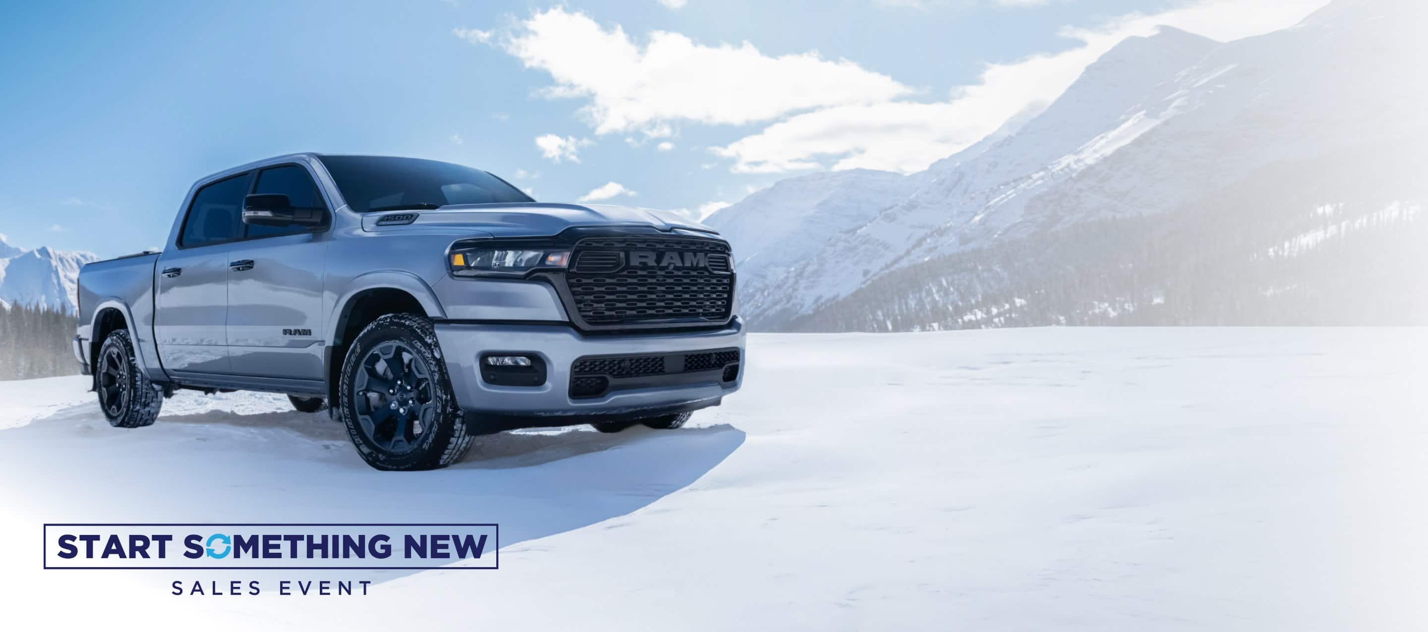 A white 2026 Ram 1500 Big Horn 4x4 Crew Cab parked on a snow-covered clearing off-road in the mountains. Start Something New Sales Event.