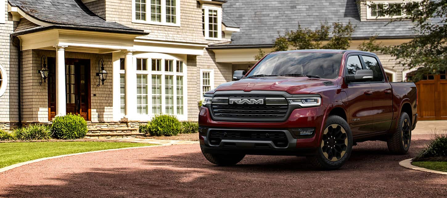 An angled driver-side front profile of a red 2025 Ram 1500 Ramcharger Limited Crew Cab, parked in the driveway of a home.