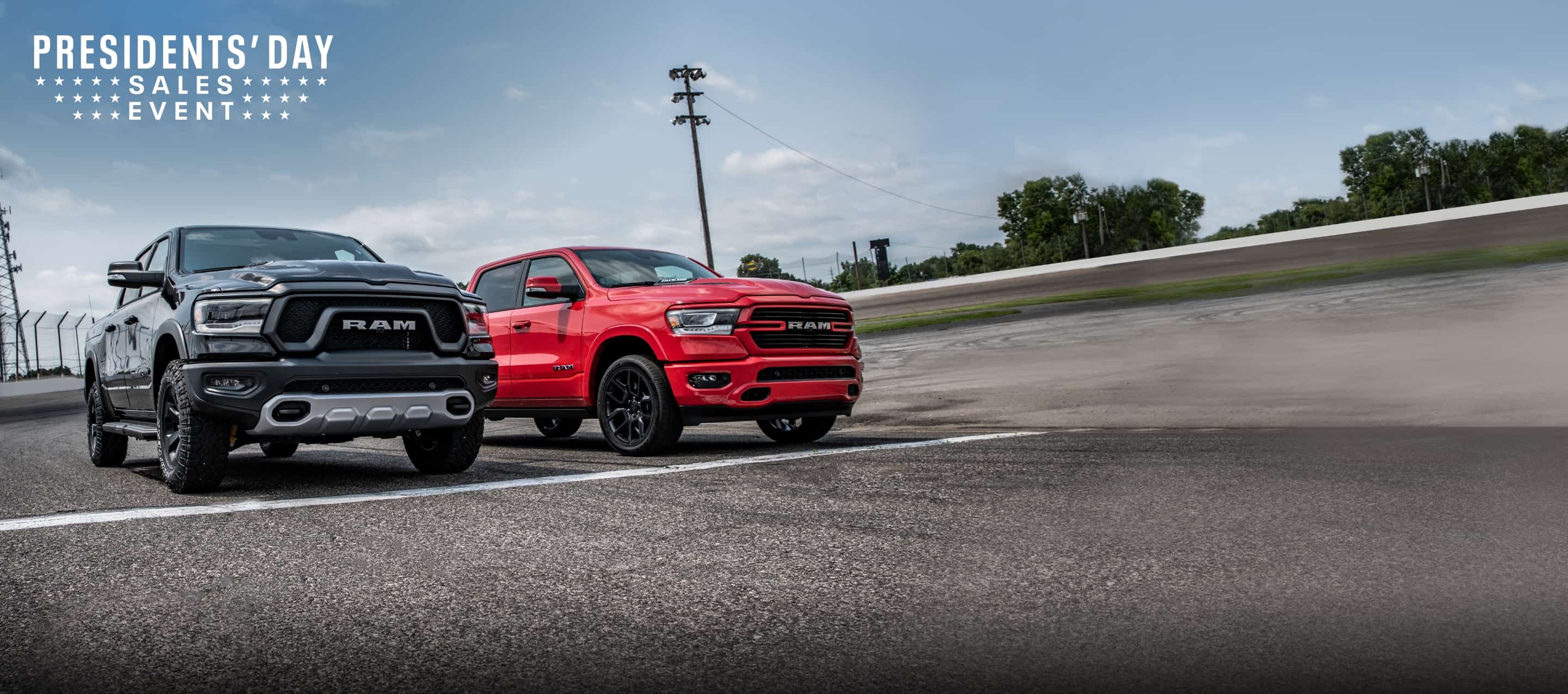 A black 2022 Ram 1500 Rebel and a red 2022 Ram 1500 Laramie at the starting line of a racetrack. The Presidents' Day Sales Event logo.