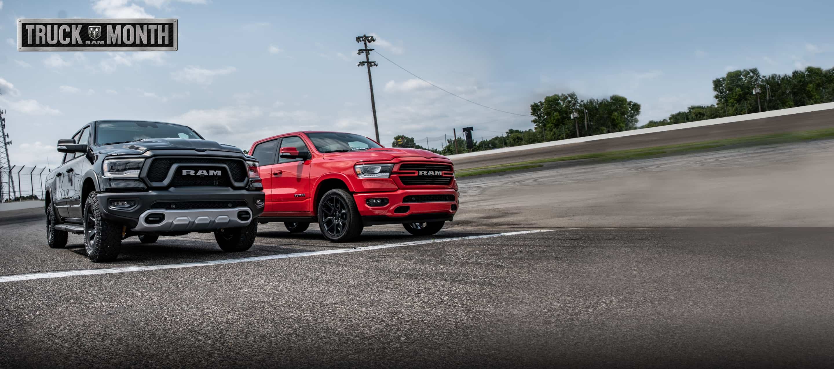  A black 2022 Ram 1500 Rebel and a red 2022 Ram 1500 Laramie at the starting line of a racetrack. The Ram Truck Month logo.