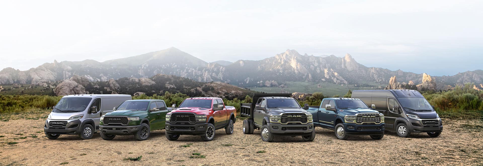 The 2026 Ram lineup: a white Ram ProMaster 2500 SLT Standard Roof Cargo Van, a green Ram 1500 Rebel 4x4 Crew Cab, a red Ram 2500 Rebel 4x4 Crew Cab, a gray Ram 4500 Big Horn Chassis Cab Crew Cab with dump body upfit, a blue Ram 3500 Limited 4x4 Crew Cab and a black Ram ProMaster 3500 SLT Plus High Roof Cargo Van, all parked side-by-side on a hilltop.