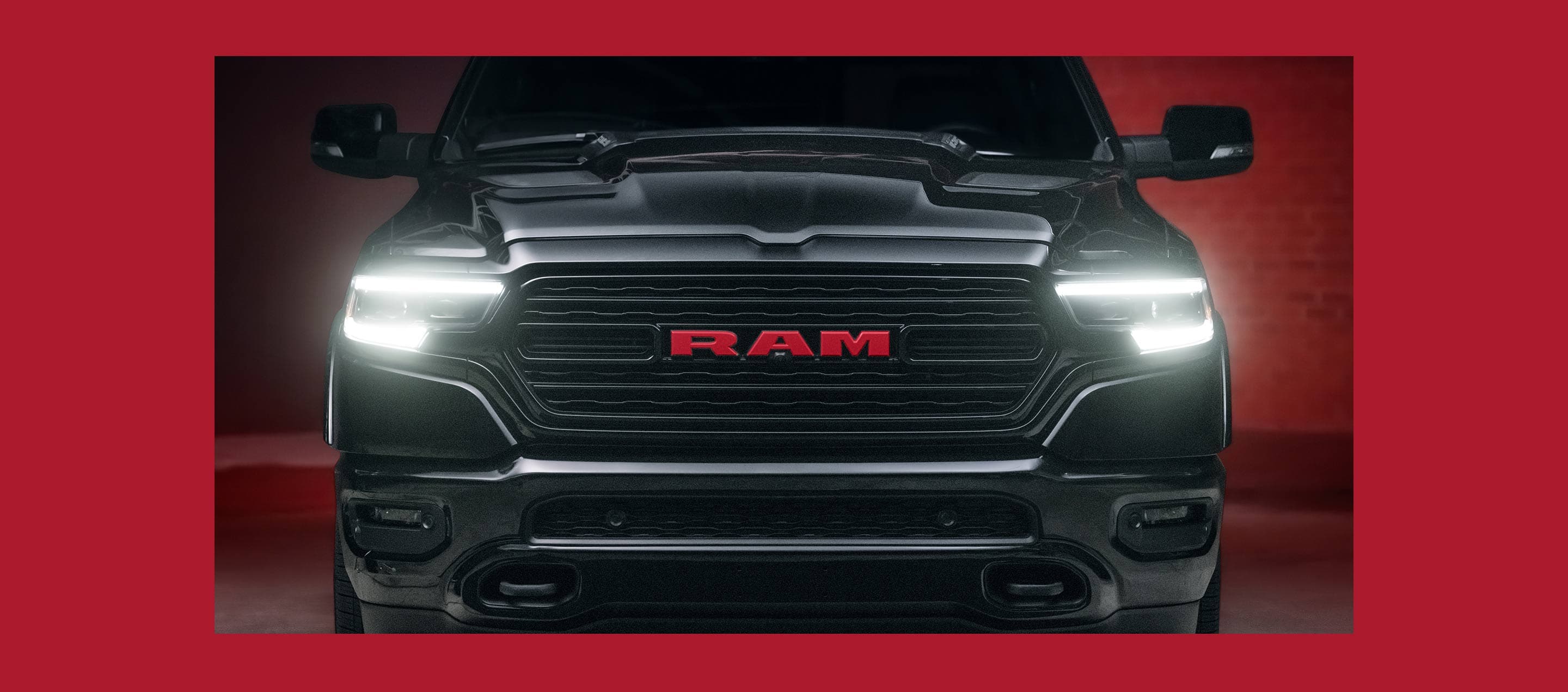 A close-up of the front end of a 2023 Ram 1500 Limited Ram Red Edition with its headlamps on.