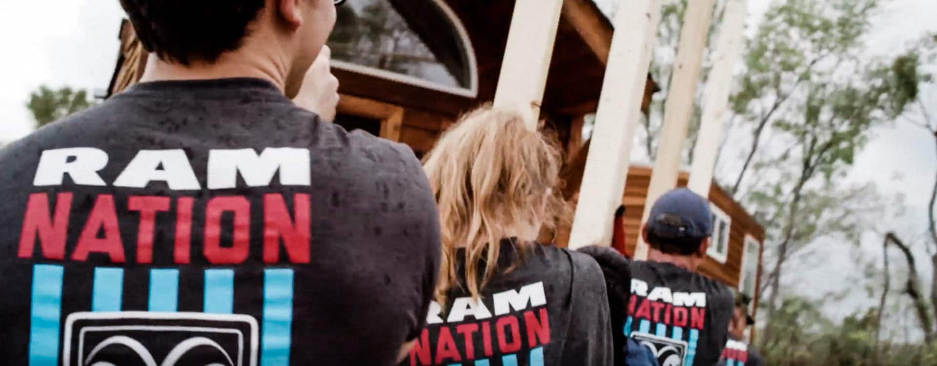 A group of volunteers wearing Ram Nation t-shirts, carrying lumber toward a home.