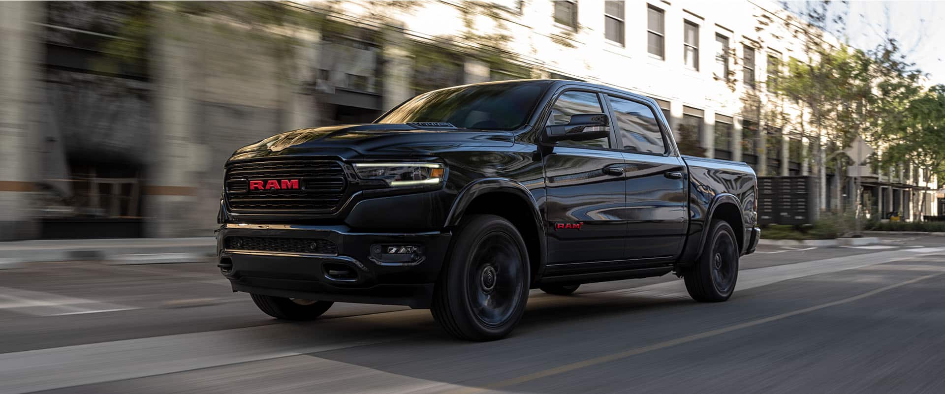 A 2023 Ram 1500 Limited Ram Red Edition being driven on a city street with the background blurred to indicate the vehicle is in motion.