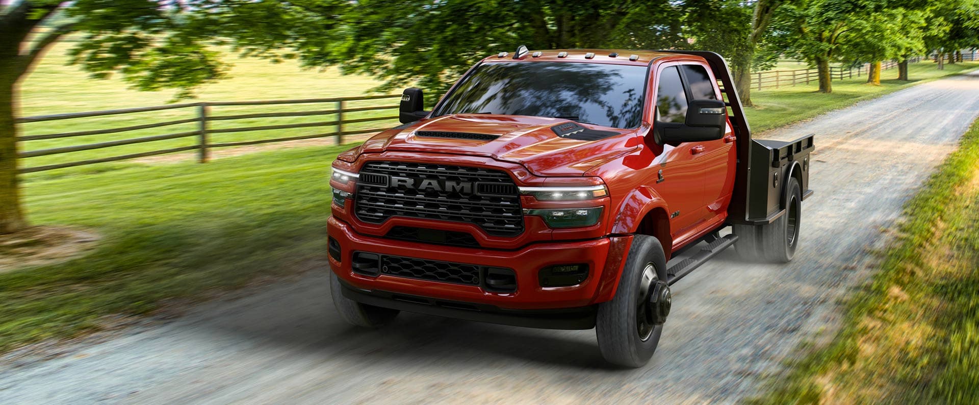 A front three-quarter view of a Flame Red 5500 Laramie Chassis Cab Night Edition being driven along a dirt road near a farm.