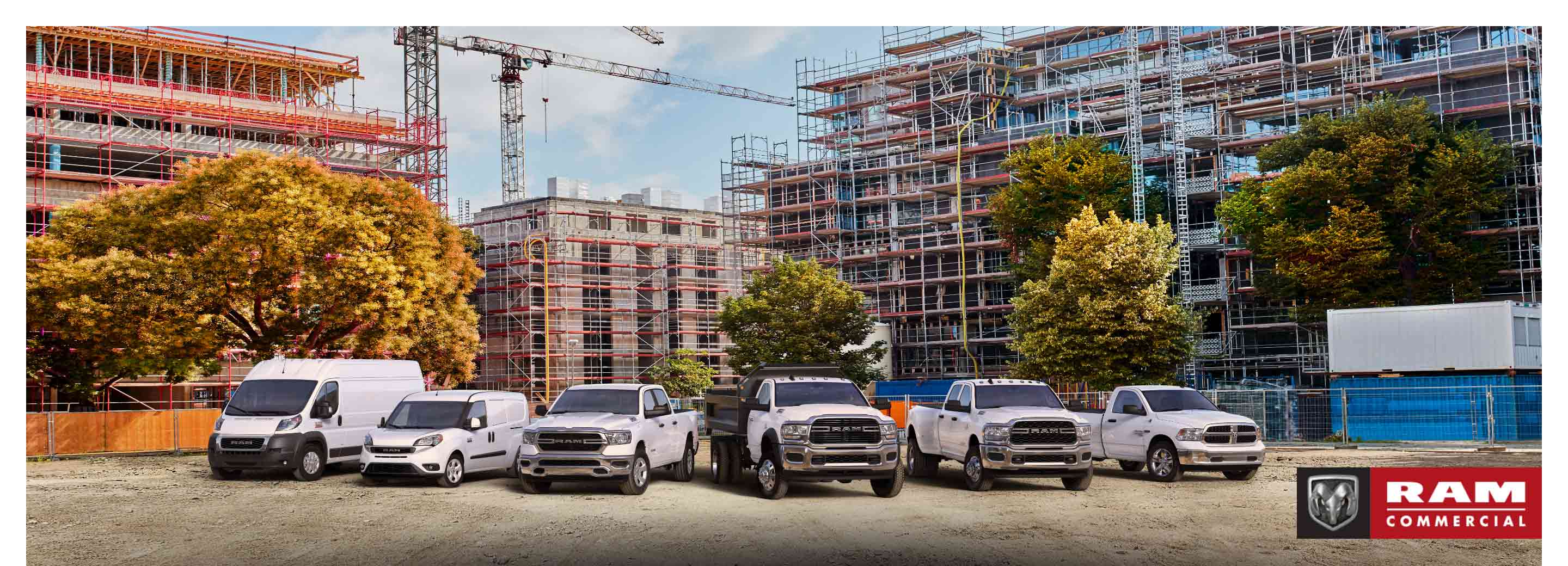 The 2021 Ram lineup parked at a massive commercial construction site. From left to right: a Ram ProMaster High Roof, Ram ProMaster City Cargo Van, Ram 1500, Ram 5500 Chassis Cab with dump body, Ram 3500 and Ram 1500 Classic. The Ram Commercial logo.