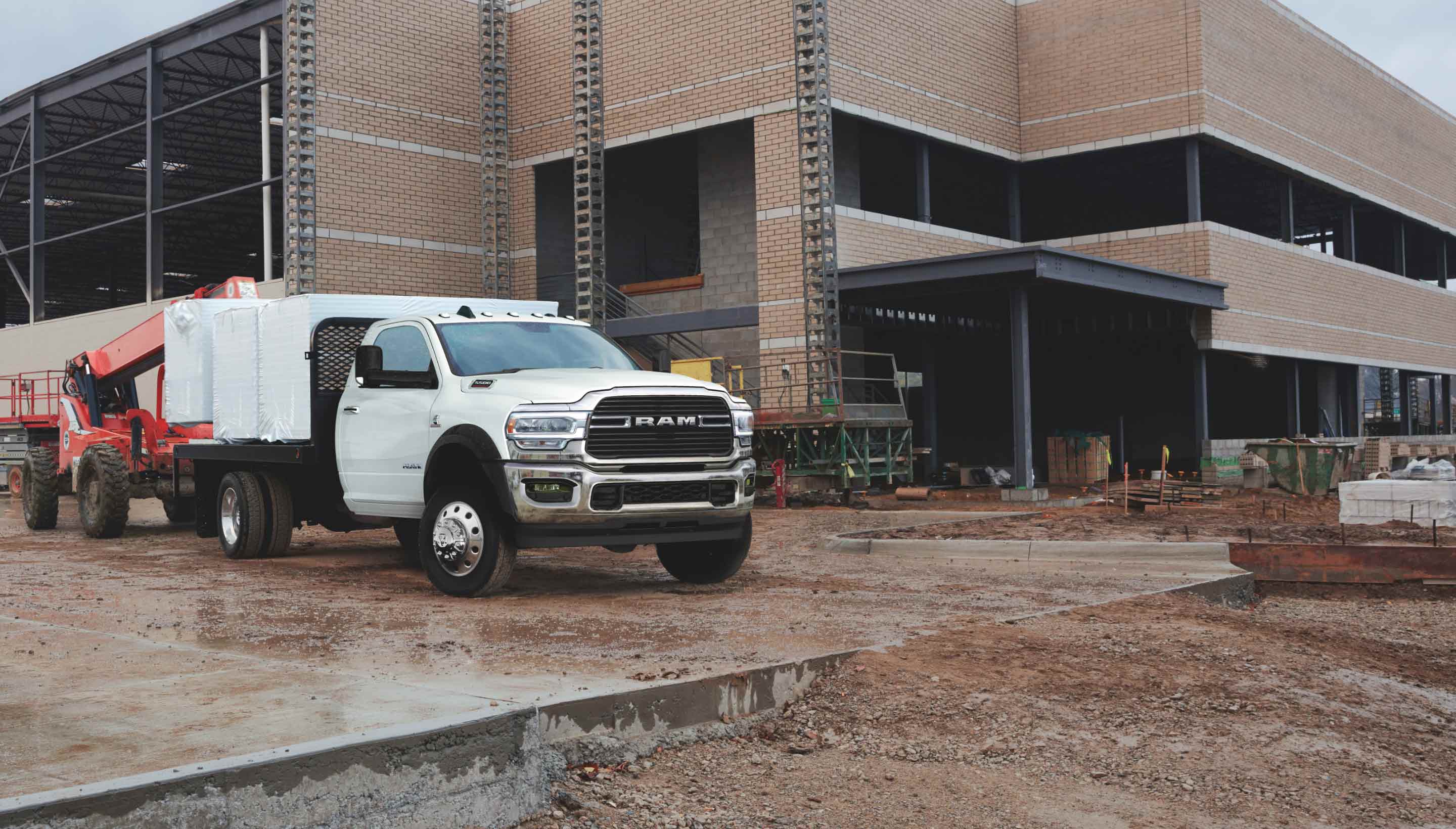 A 2022 Ram Chassis Cab on a construction site, with a boom lift loading tightly wrapped pallets onto the truck flat bed.