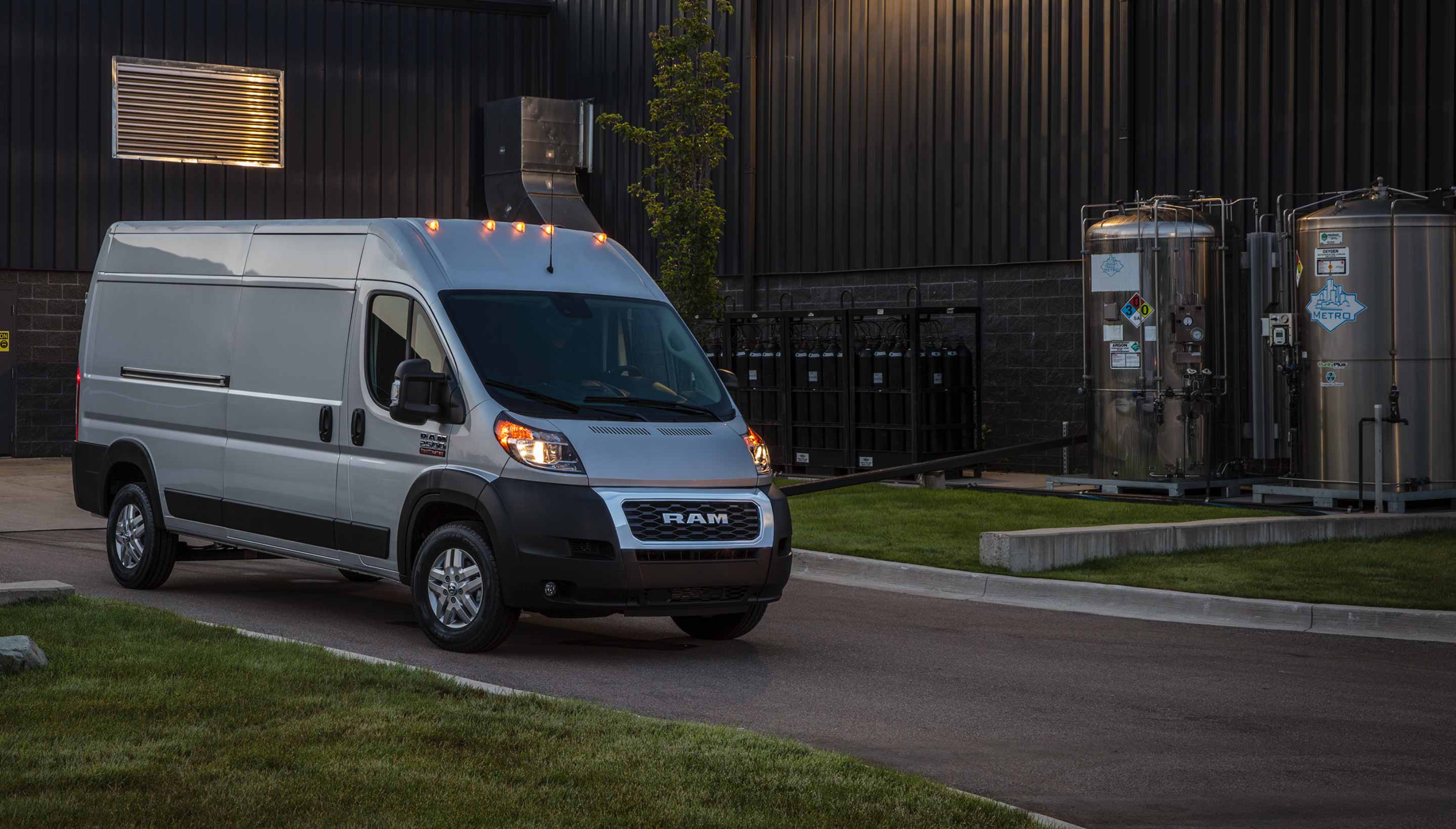 A 2022 Ram ProMaster with its headlamps lit, parked in a driveway at dusk.