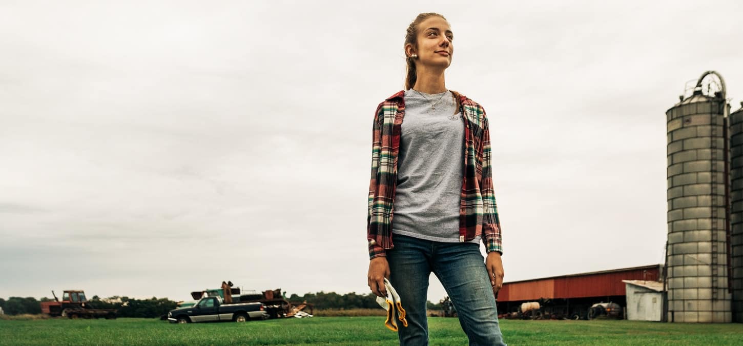 Grayce Emmick standing proudly on her farm with her Ram truck in the background.