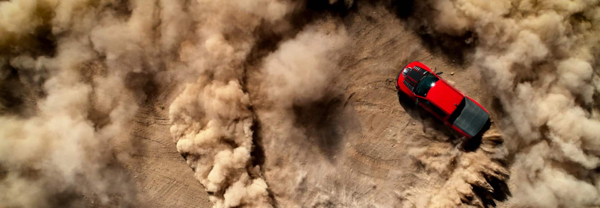 An overhead view of a red 2021 Ram 1500 TRX creating doughnuts in the sand, kicking up clouds of dust.