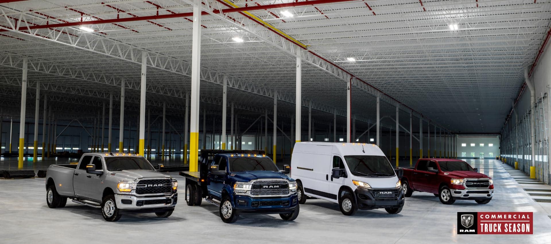 A lineup of four Ram Brand vehicles parked in an industrial garage. From left to right: a silver 2024 Ram 3500 Big Horn 4x4 Crew Cab, a blue 2024 Ram 4500 Limited Chassis Crew Cab with utility bed upfit, a white 2024 Ram ProMaster 2500 Tradesman 159" WB High Roof Cargo Van and a red 2024 Ram 1500 Tradesman 4x4 Crew Cab. Ram Commercial Truck Season.