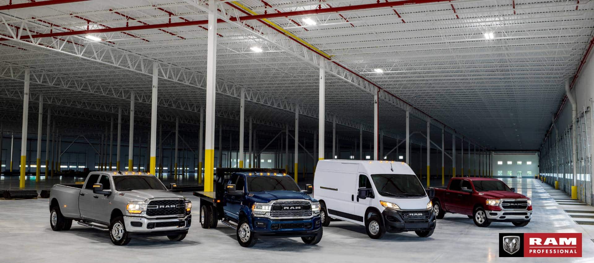 A lineup of four Ram Brand vehicles parked in an industrial garage. From left to right: a silver 2024 Ram 3500 Big Horn 4x4 Crew Cab, a blue 2024 Ram 4500 Limited Chassis Crew Cab with utility bed upfit, a white 2024 Ram ProMaster 2500 Tradesman 159" WB High Roof Cargo Van and a red 2024 Ram 1500 Tradesman 4x4 Crew Cab. Ram Professional.