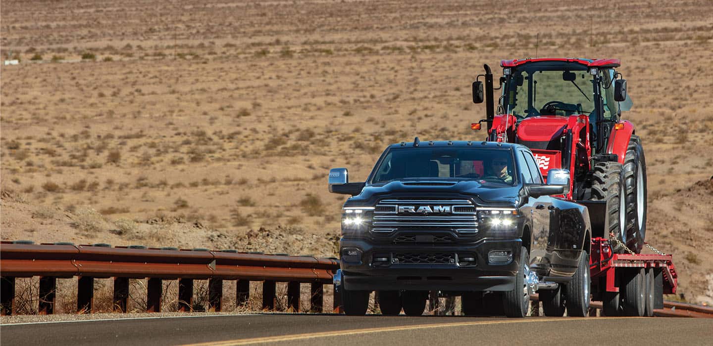 A Ram truck towing a piece of farm equipment on a trailer.