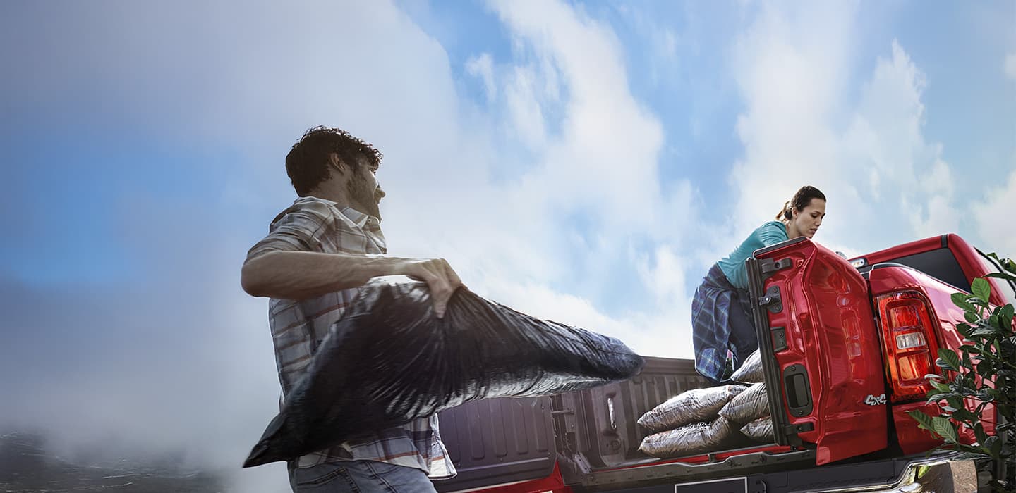 Two people loading bags of mulch into the bed of a Ram truck.