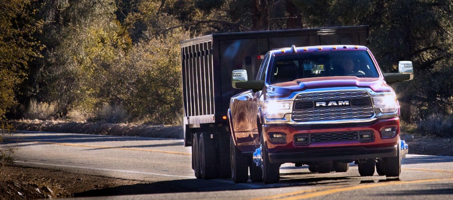 A red 2024 Ram 3500 Limited 4x4 Crew Cab being driven on a highway towing a dump body trailer.