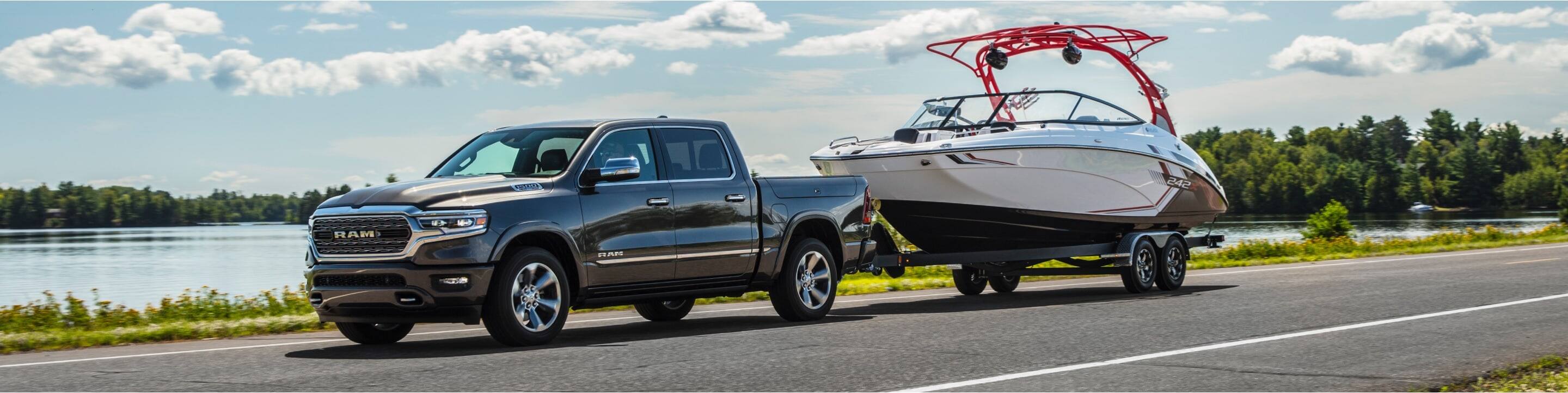 A 2021 Ram 1500 towing a boat and being driven on a highway next to a body of water.
