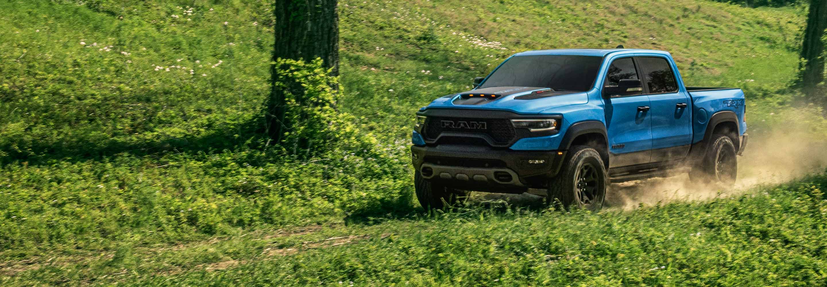 The 2023 Ram 1500 TRX being driven on a rough trail through the grass, dust rising from its wheels.