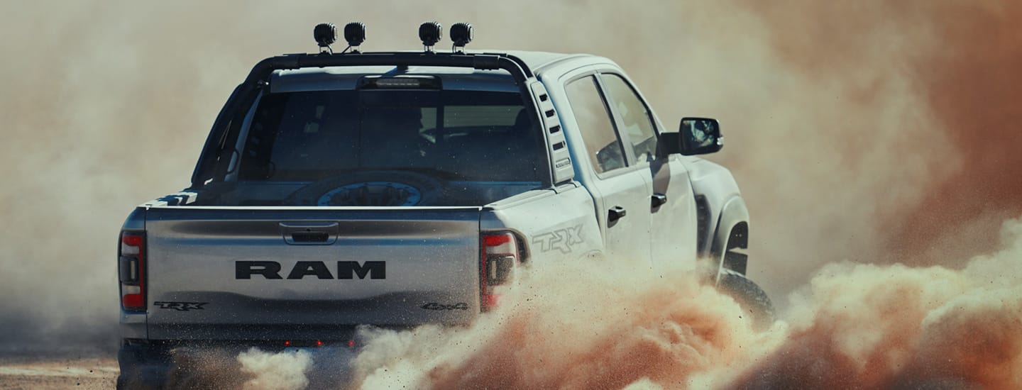 A rear view of the 2023 Ram 1500 TRX surrounded by a billowing cloud of dust coming from its wheels.