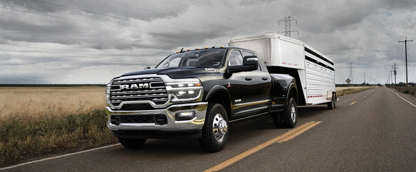 A driver-side front angle of a black 2025 Ram 3500 Limited 4x4 Mega Cab towing a large fifth-wheel trailer.