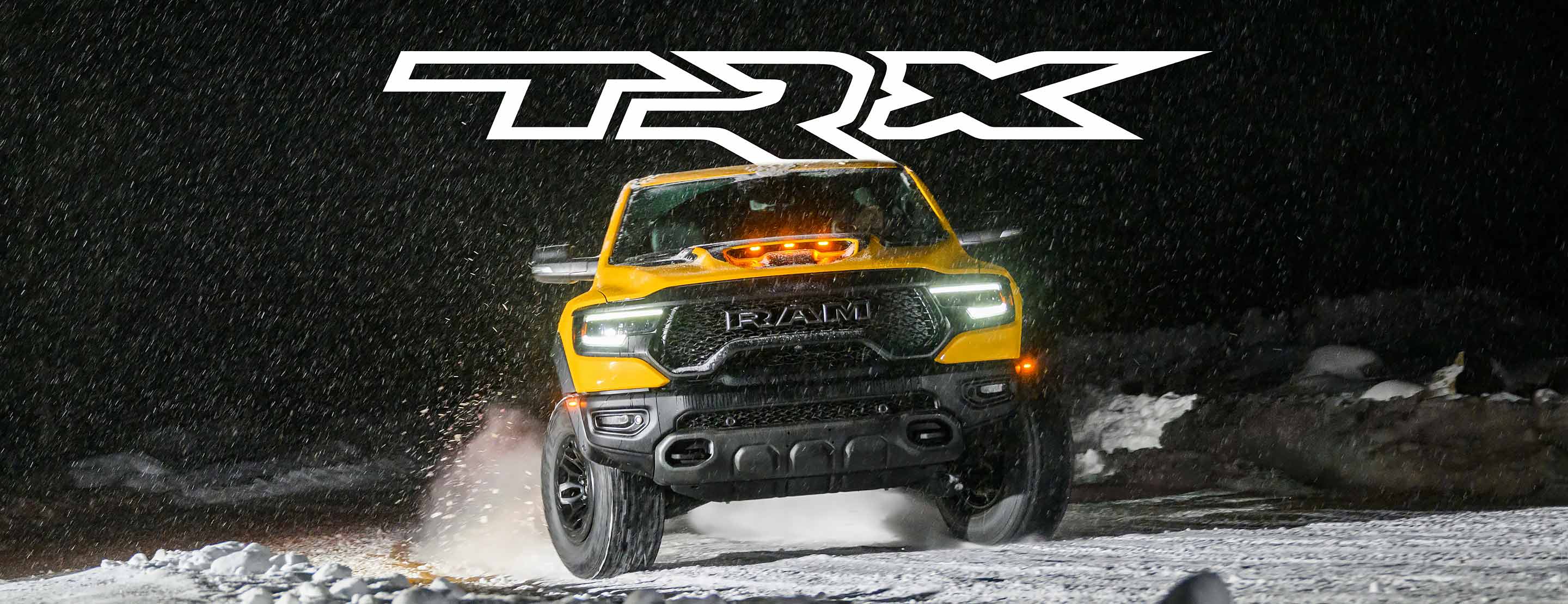 TRX. A head-on angle of a yellow 2023 Ram 1500 TRX Havoc Edition being driven at night, kicking up snow with its tires.