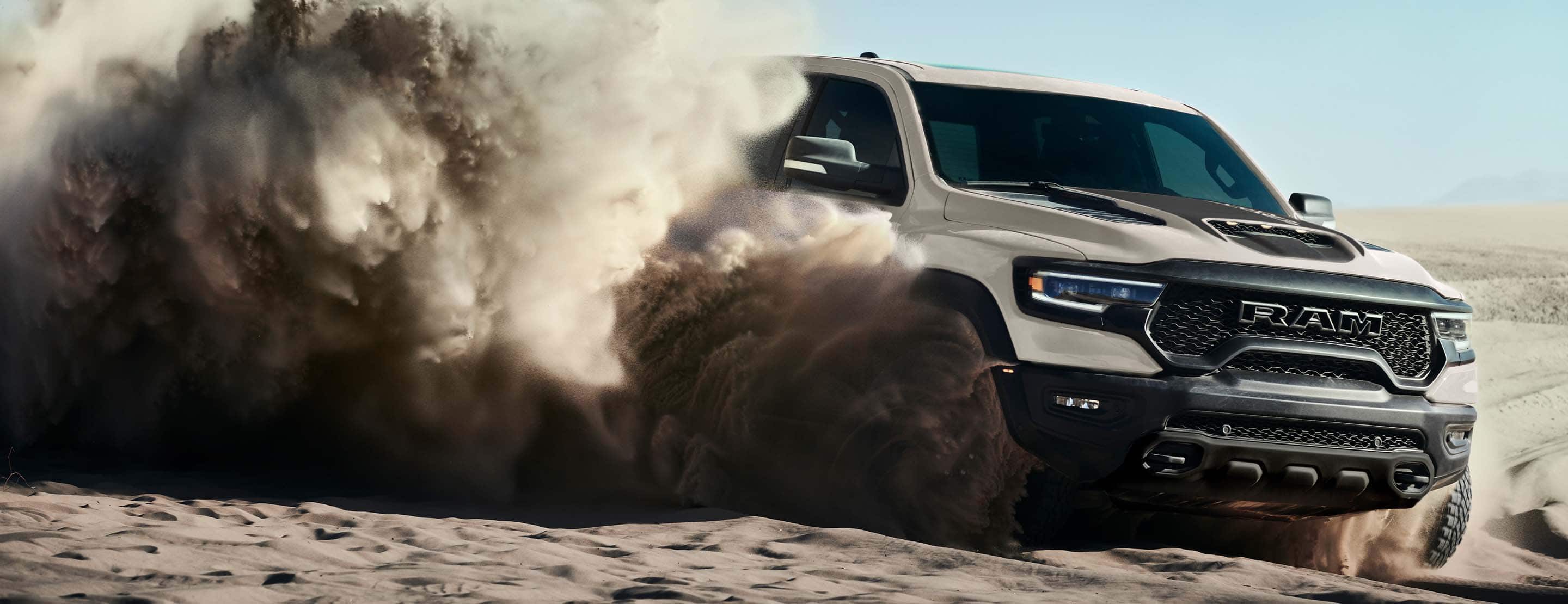 The 2022 Ram 1500 TRX Sandblast Edition being driven on sand with billowing clouds obscuring the rear of the vehicle.
