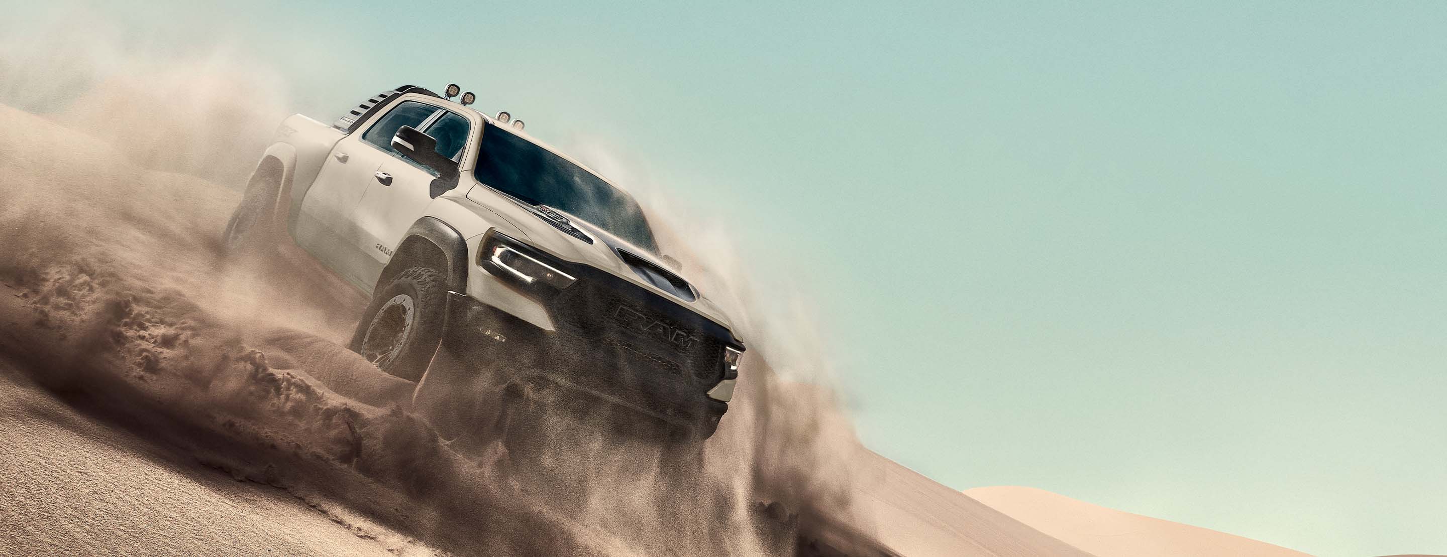 The 2022 Ram 1500 TRX Sandblast Edition being driven in the desert with clouds of loose sand billowing around the vehicle.