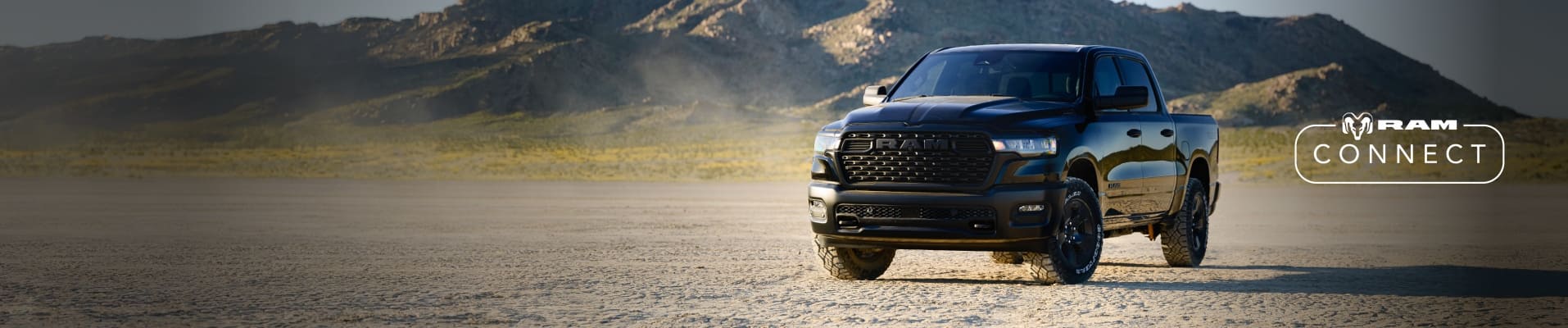 A driver-side front angle of a black 2026 Ram 1500 Warlock Crew Cab parked on a clearing with mountains in the background. The Ram Connect logo.