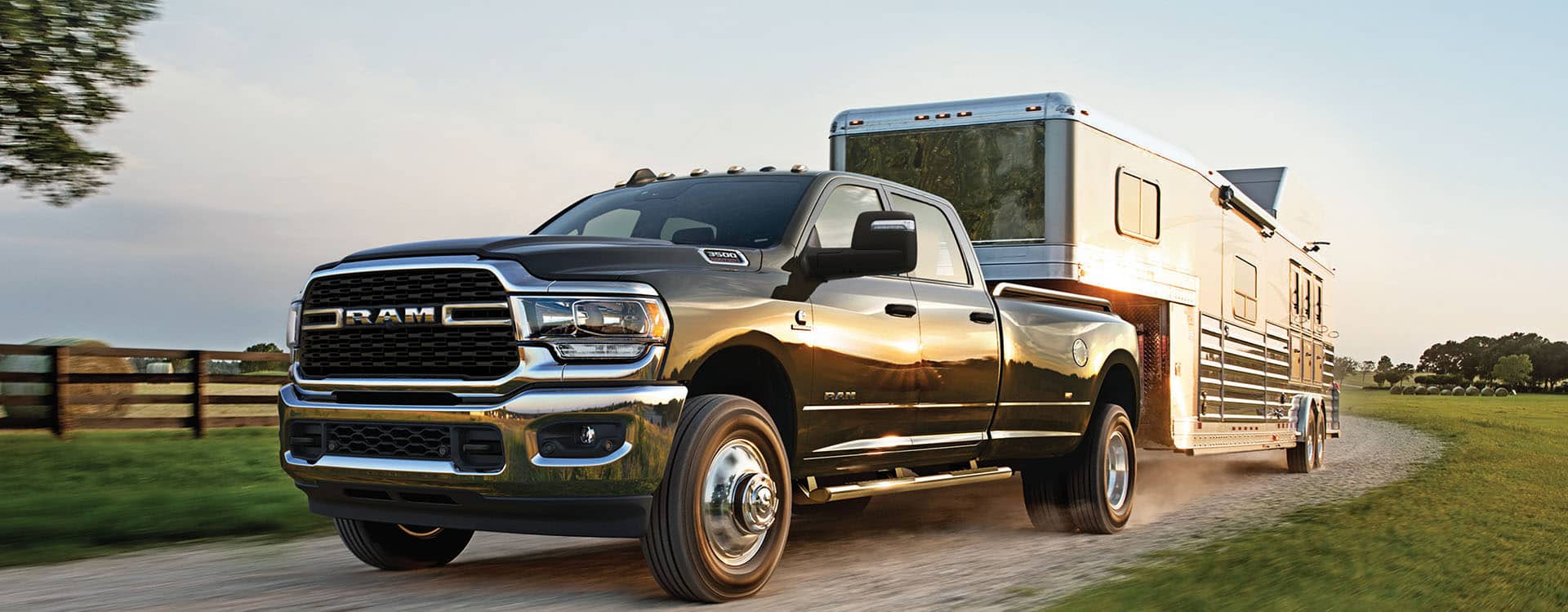 A driver-side front angle of a black 2024 Ram 3500 Big Horn 4x4 Crew Cab towing a fifth wheel travel trailer.