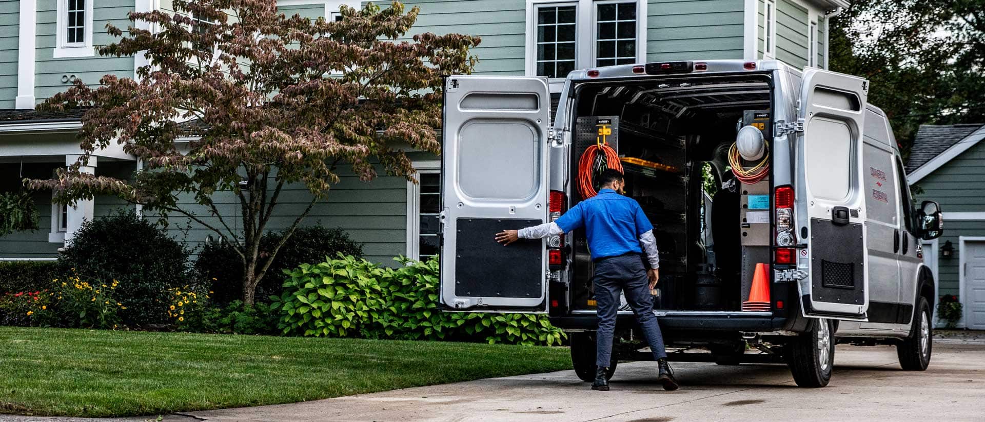 A 2021 Ram ProMaster 1500 with an electrician upfit, its rear doors open—revealing a cargo area full of equipment, parked in the driveway of a home.